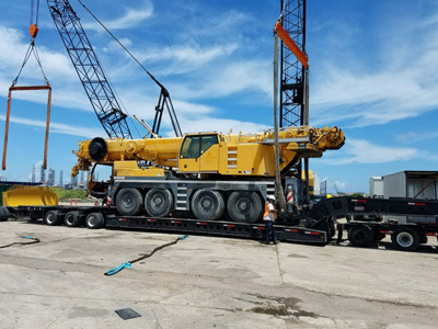Export Logistics & Shipping, Inc. lifts Liebherr LTM1100 crane from flat rack using two cranes